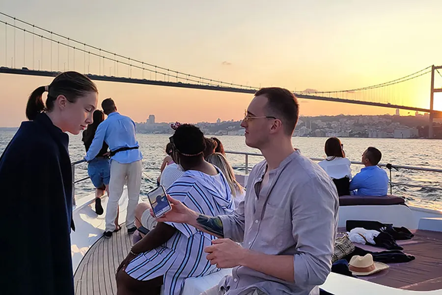 Friends on the yacht deck under the Bosphorus Bridge at sunset