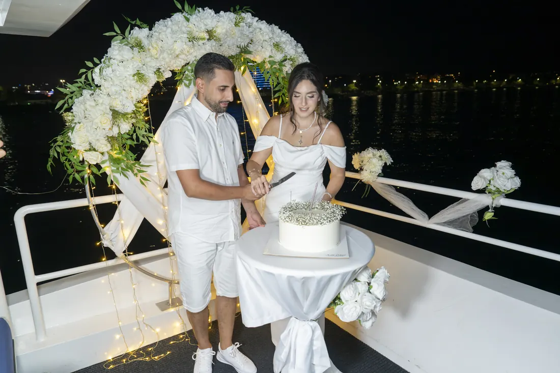 Newlyweds cutting the cake under a flower arch on a yacht